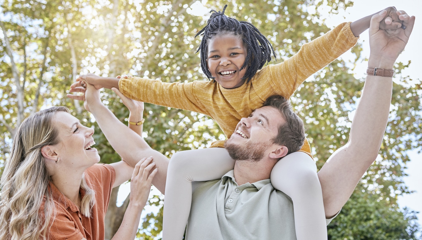 Family, adoption and piggyback in the park with a girl and foster parents having fun together in the park. Diversity, playful and freedom with a mother, father and daughter bonding outdoor in nature