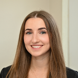 Portrait of a smiling woman with long brown hair, wearing a dark top, looking at the camera.